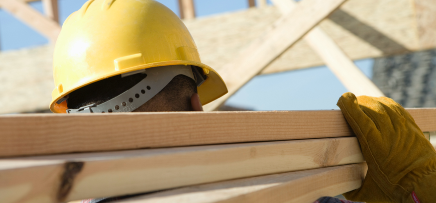 Photo of a construction worker in a hard hat carrying a few 2x4s across his shoulder.